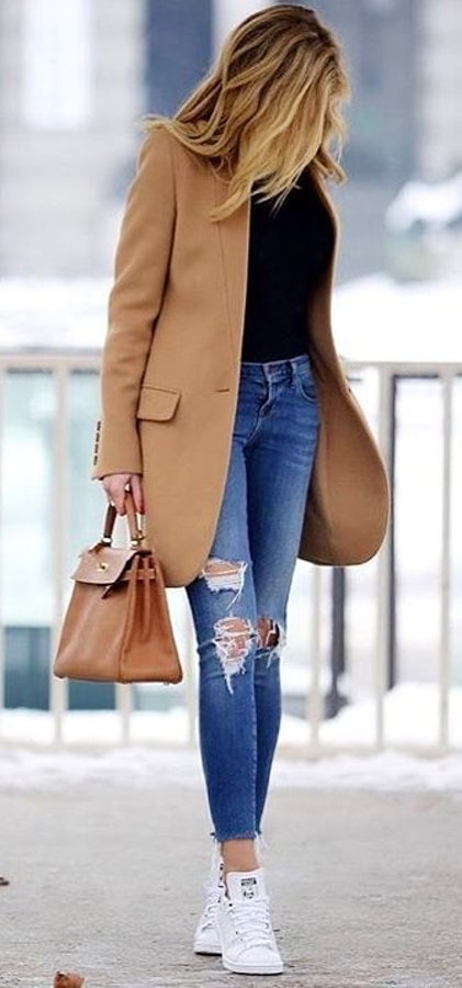 Women's brown blazer, black undershirt, distressed blue jeans, white shoes, and brown handbag outfit.