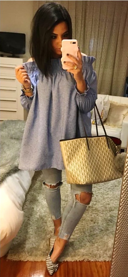 Women's gray long sleeve off-shoulder top and blue distressed jeans.