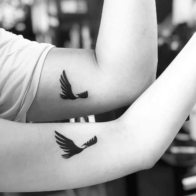 Matching flying birds arm tattoos.